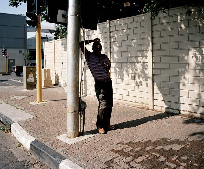 Photographed in South Africa, a man stands in the shade, sheltering from the intense heat