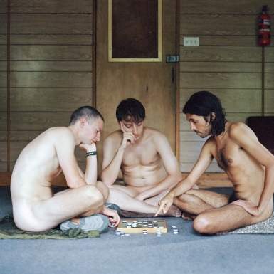 Three nudists sit and play board game.