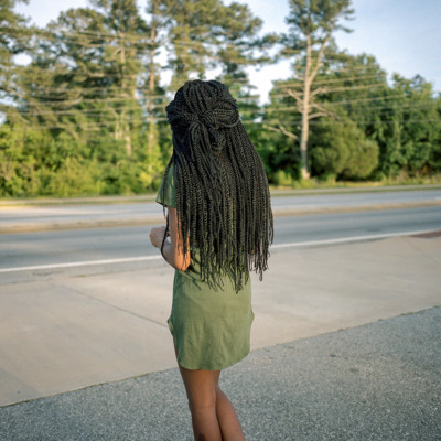 A girl with long braids and a green dress, with her back to the camera,