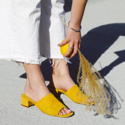 A woman reaches down to the dry, dusty floor, she's holding a lemon and a brush of twigs that match her yellow sandals.