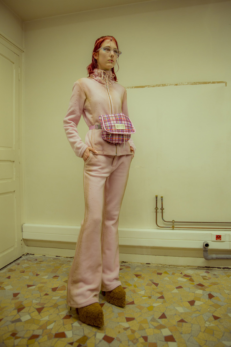 A girl with red hair poses in a pink set with platform brown shows and a pink large fanny pack around waist.