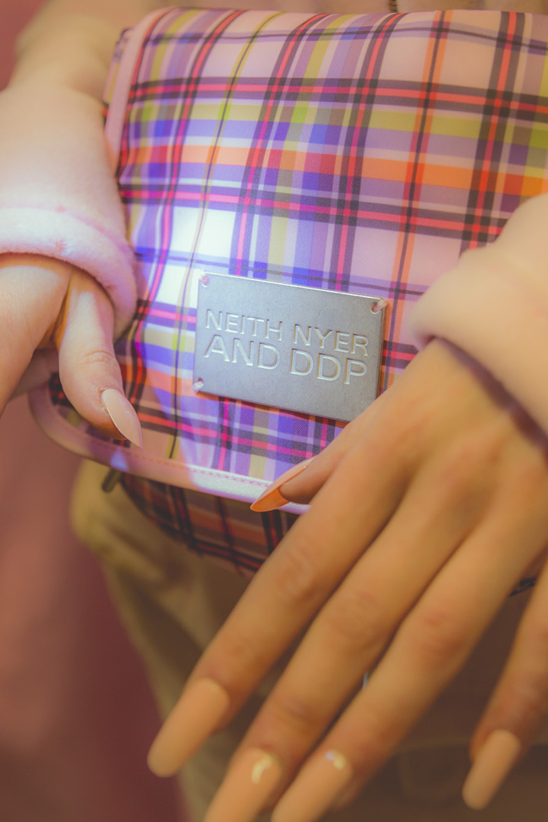 A close up of pink plaid fanny pack, hands with almond shaped pink nails in shot.