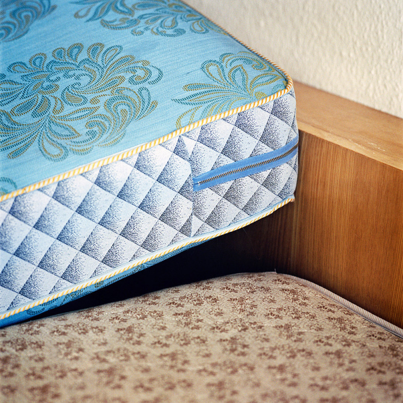 A bright, tacky mattress leans against a wall, an ominous dark gap fills the space between them.