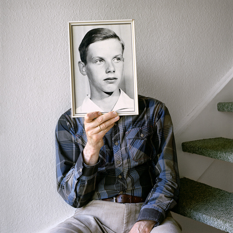 A man holds an old black and white photograph of young boy in front of his own face.