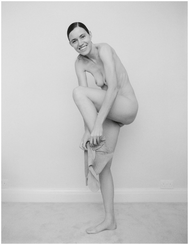 a naked girl standing up smiling, pulling up her stockings