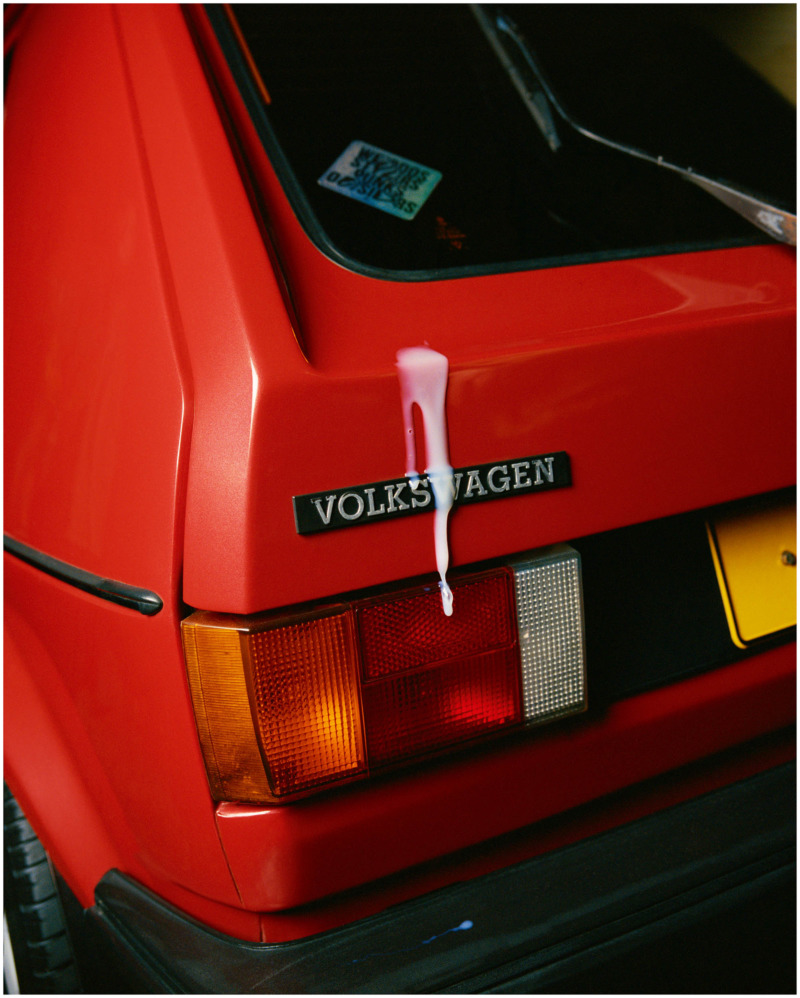 the back left corner of an old volkswagen golf, brightly light and with a white liquid running down the back