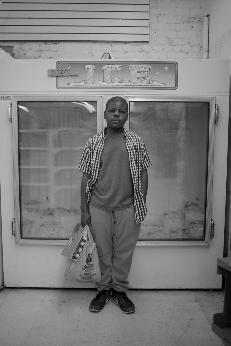 A young boy holding a shopping bag, standing in front of an ice fridge.