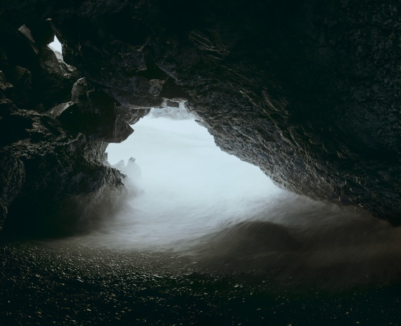 Standing inside an empty sea cave, the camera peeks out onto the waves.