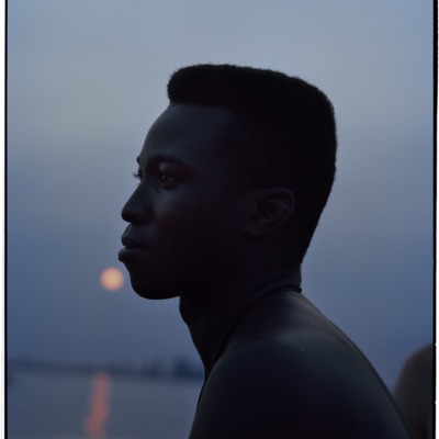 A portrait of a black man in profile, set against the lilac sky and the rose gold setting sun.