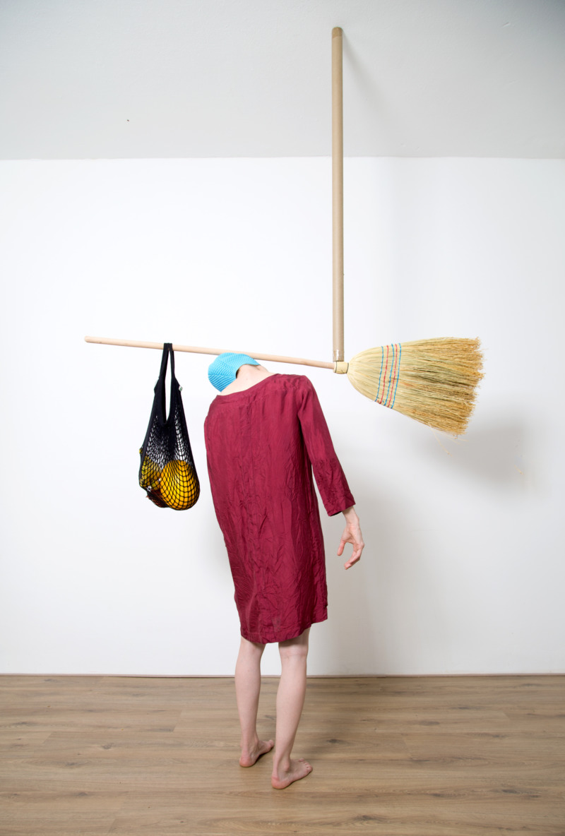 A person carries a broom and a bag of stuff over their shoulders.