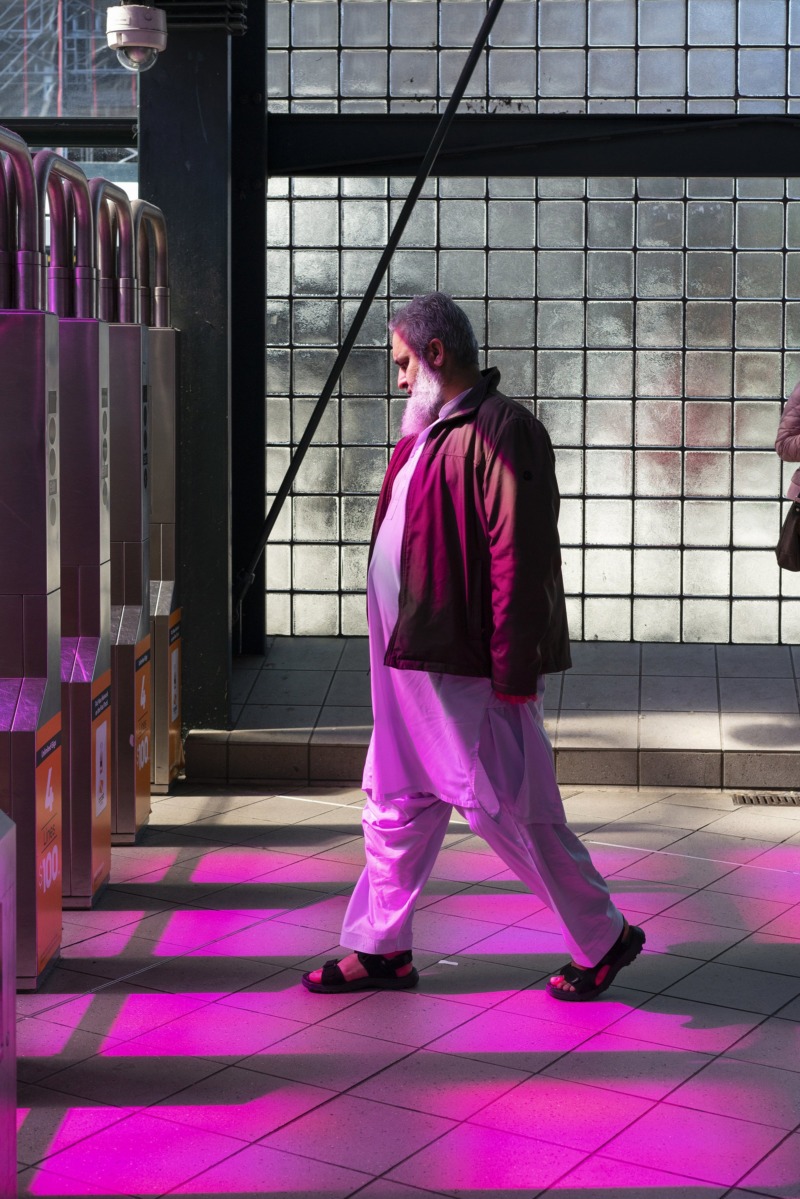A middle aged man in Muslim dress walks through purple light.