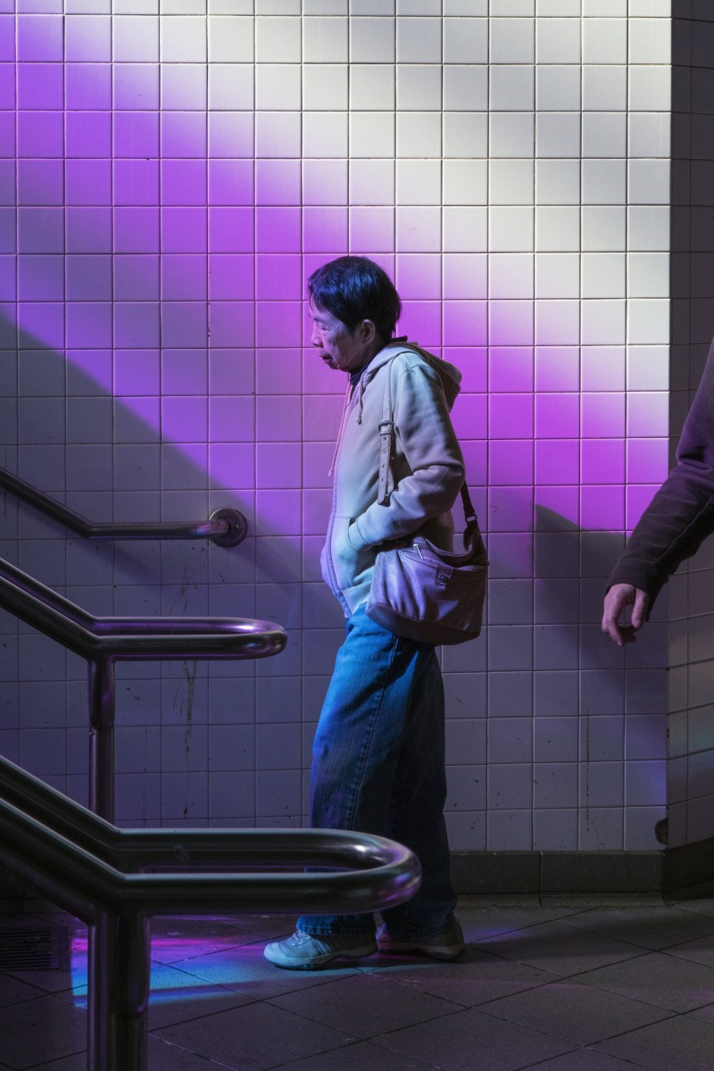 A lone man bathed in purple light descends the station stairs.