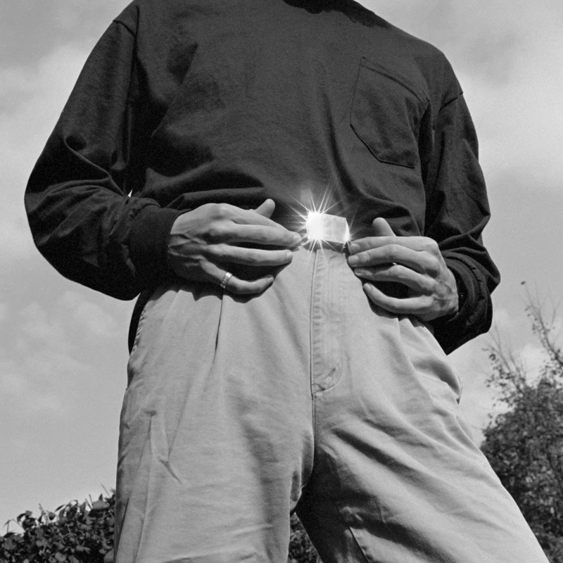 A man rests his hands on his belt, the sun shines from its buckle.