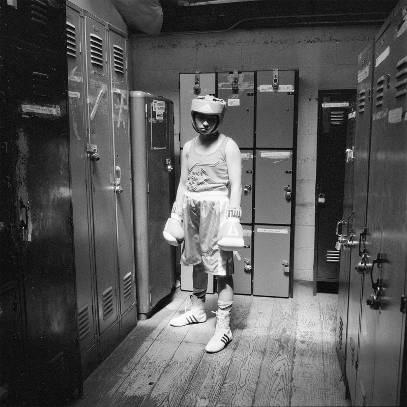A boxer stands in full safety gear amongst the lockers of the changing room.
