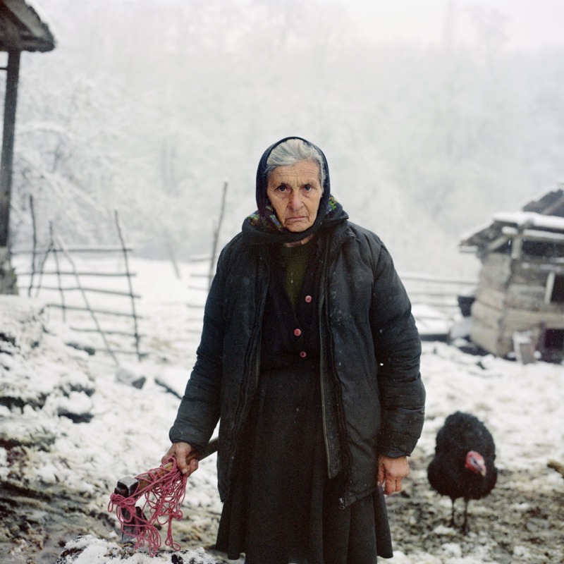 An old babushka stands square to the camera, an axe in her hand.