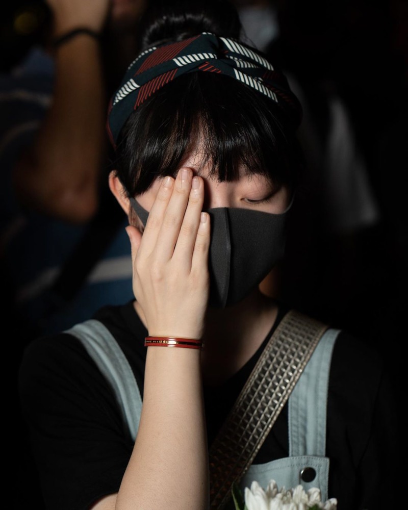 A young woman covers her face with a mask and a hand.