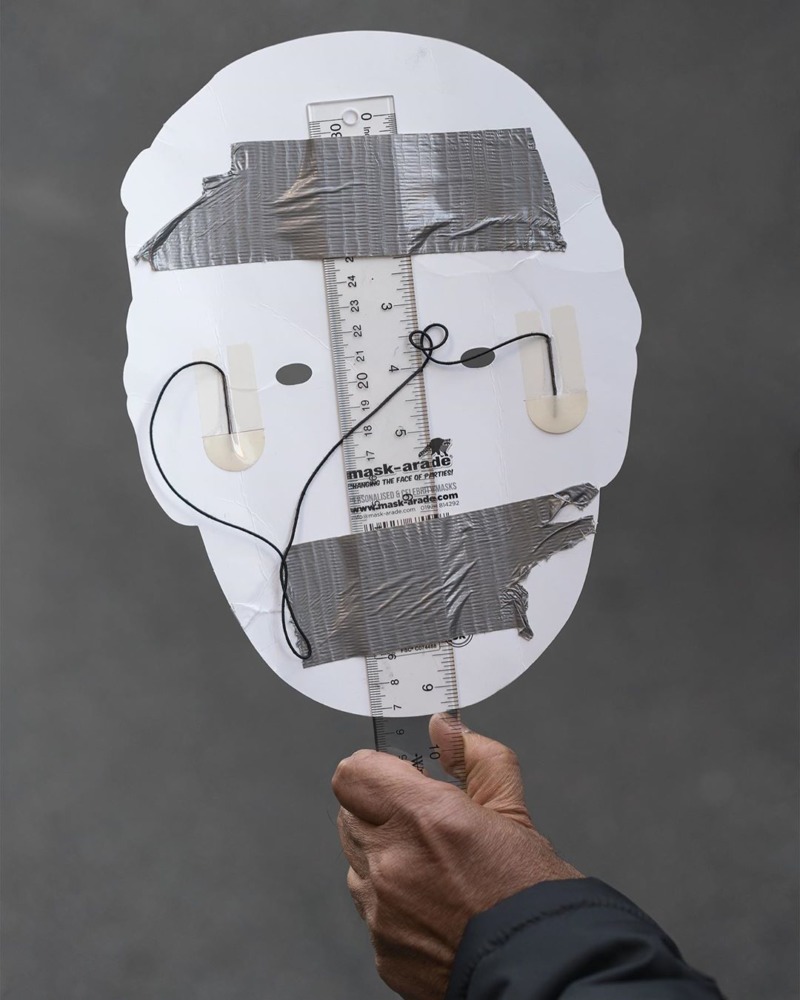 The back of a paper mask, selotaped to a ruler.