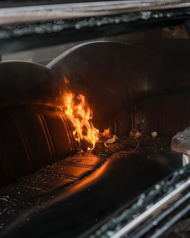 A fire burns on the leather seat of a smashed up car.