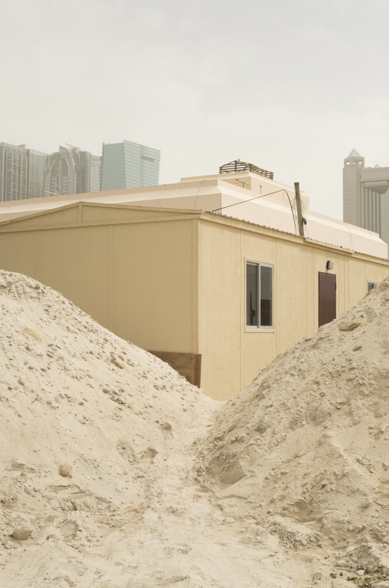 A low house appears almost buried between piles of sand.