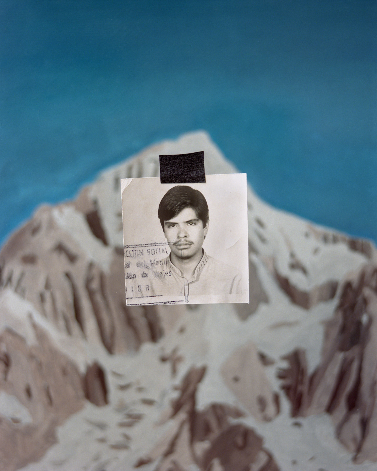 An old passport photo has been cut out and pasted on top of an image of a snow-capped mountain.