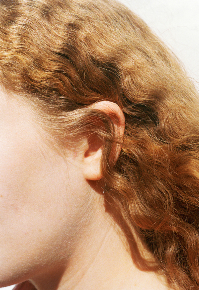 A woman's head in profile with a sweep of curly red hair that covers a gold star earring.