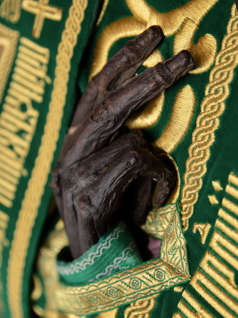 The black, dessicated hand of a saint, dressed in finery.