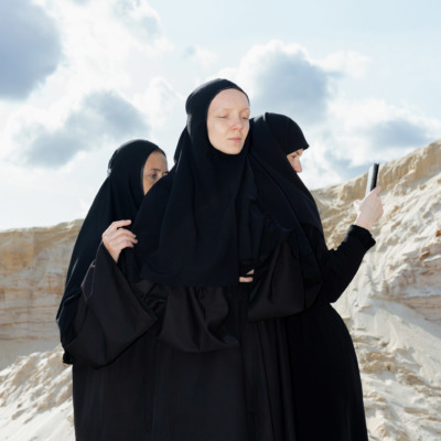 Three religious women stand in a desert, one with a cameraphone.