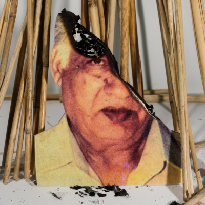 A headshot of an old man has been partially burnt and propped against a pile of bamboo.